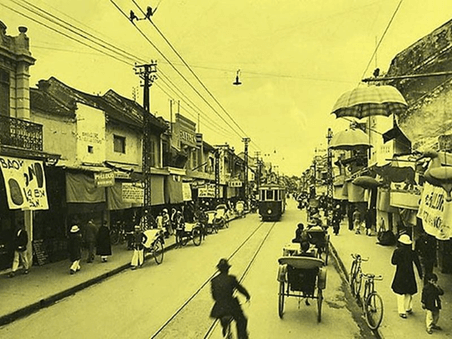 Dưới đây là hình ảnh một góc phố Hà Nội thời Pháp thuộc. Hãy quan sát và nêu nhận xét của bạn về trang phục, xe cộ và nhà cửa trong hình. (ảnh 1)